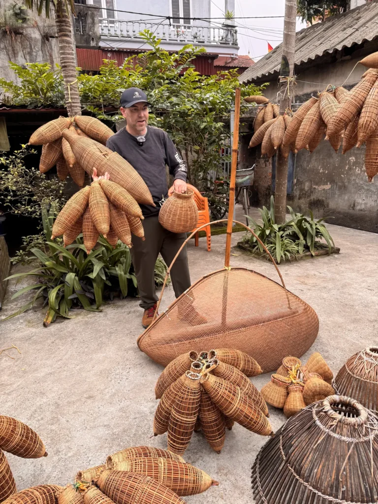 DH Garden Centre owner holding bunches of handwoven bamboo baskets in a village courtyard in Vietnam