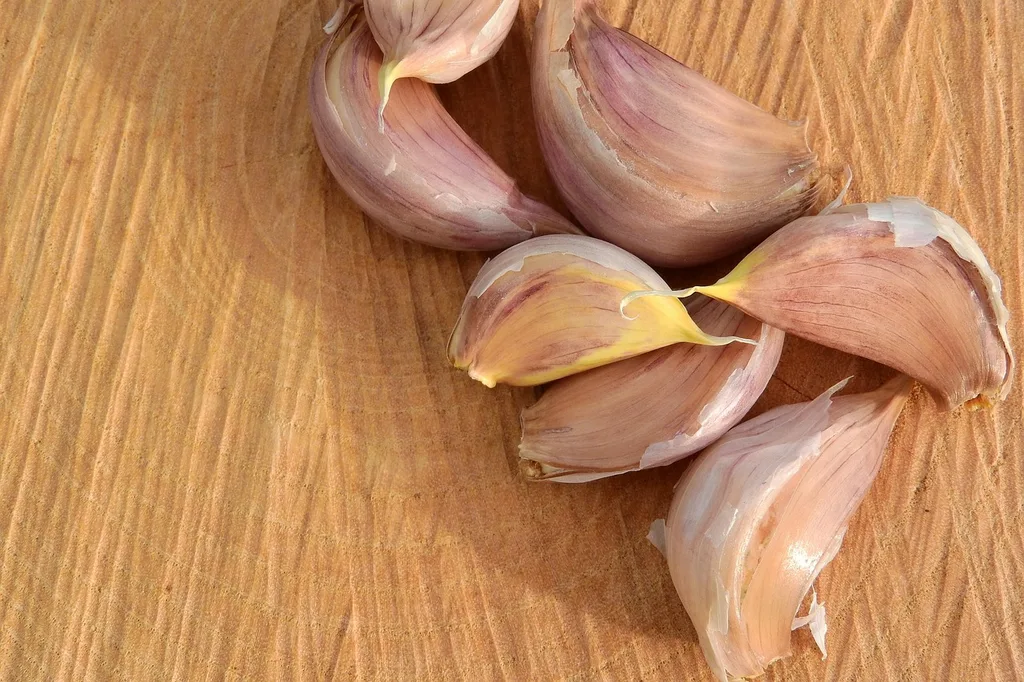 Several unpeeled garlic cloves on a wood surface, two showing a small yellow sprout at the tip